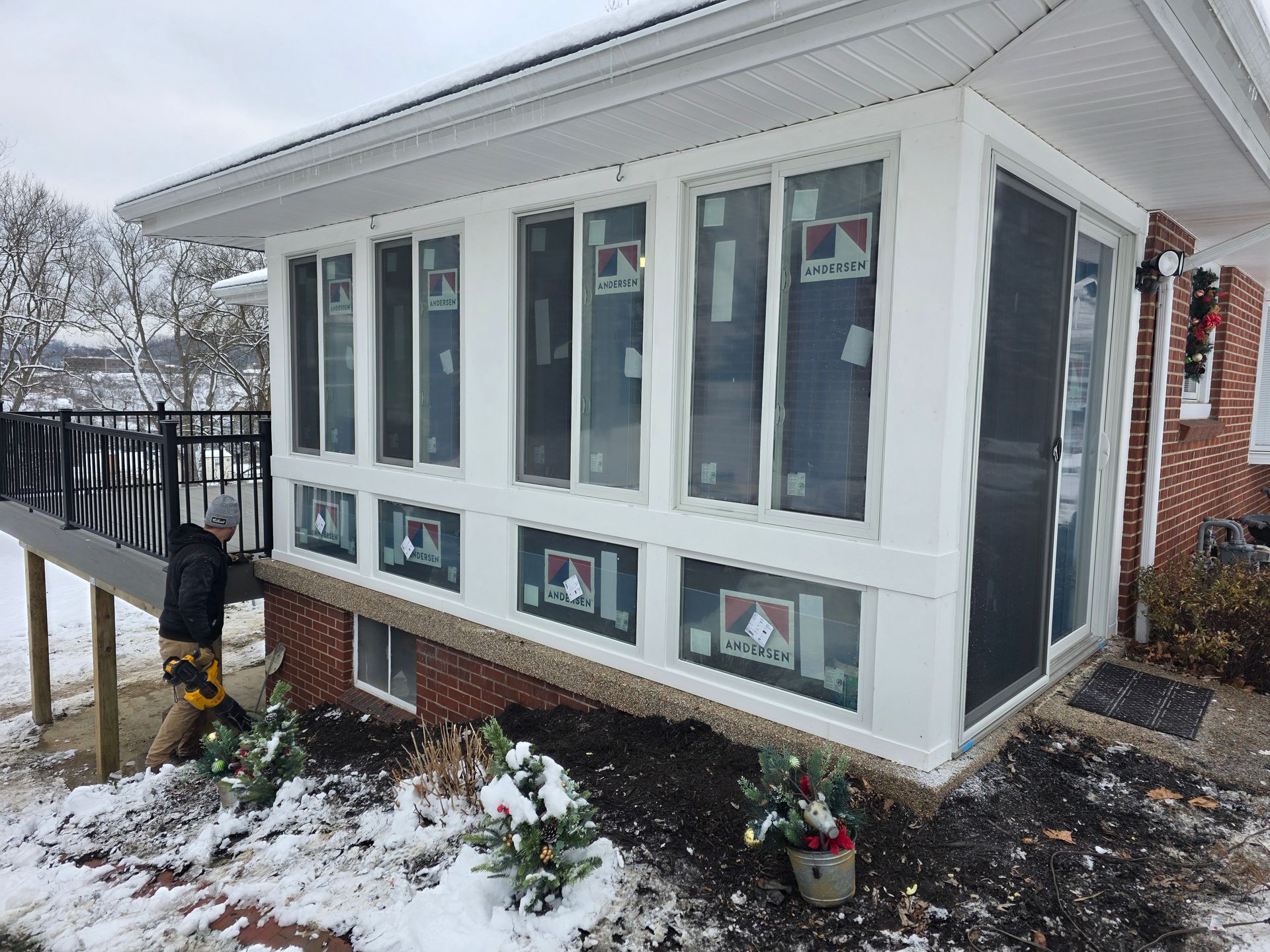 Sunroom with white trim, windows, and brick base, next to a deck with snow on the ground.