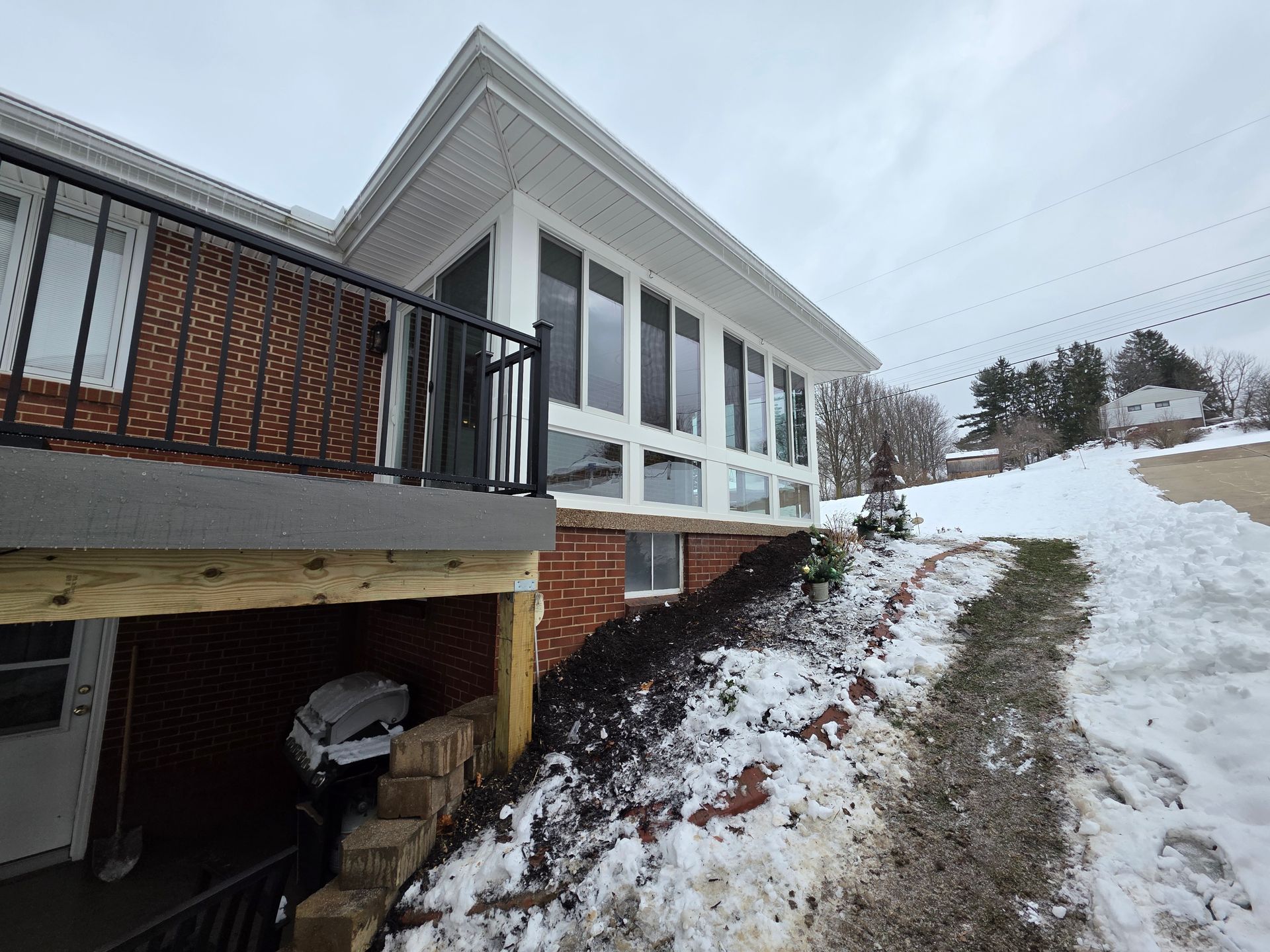 House exterior with a brick facade, glass windows, and a snow-covered driveway.
