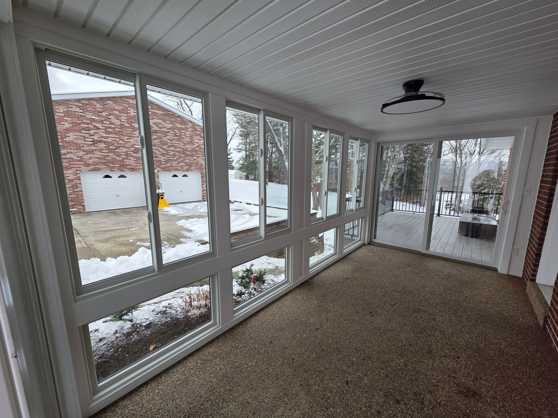 Sunroom with white-framed windows overlooking snowy outdoor scene.  Brick walls, textured floor, and a ceiling fan are visible.