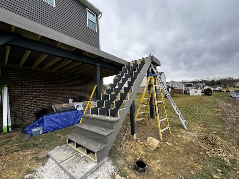 Construction of outdoor stairs leading from a gray deck down a grassy slope, with yellow ladder nearby.