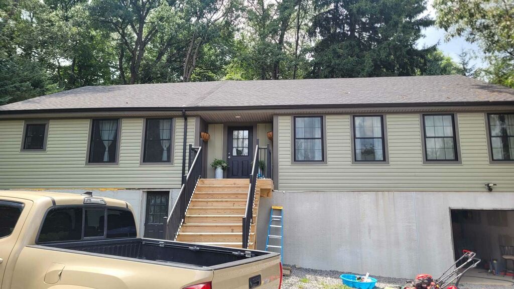 Beige house with black trim and door, wooden steps, and a tan truck in front.