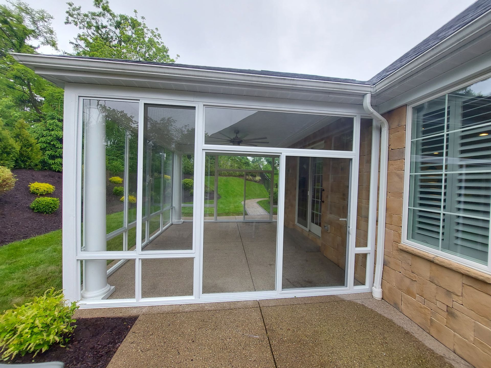 Screened-in patio with white frame, clear panels, and a concrete floor. Adjacent to a brick wall with a window.