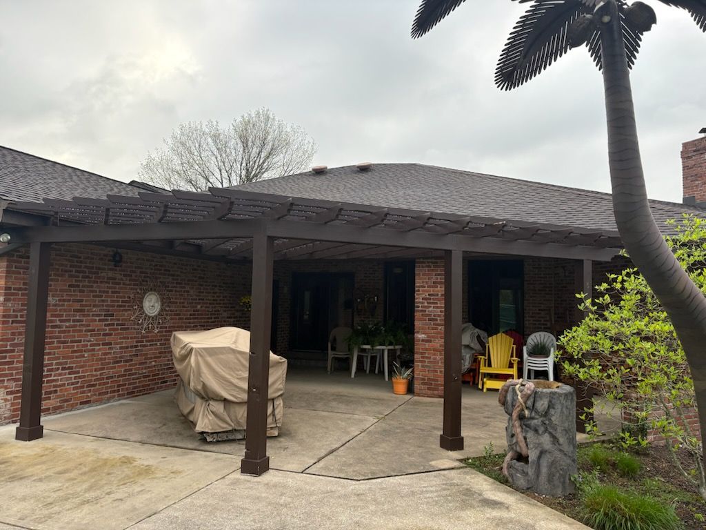 Pergola attached to a brick home. A covered patio with furniture, a statue, and a metal palm tree.