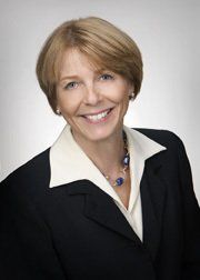 Smiling woman with blonde hair, in a black suit jacket and white collared shirt.