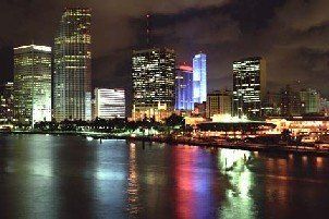 Night view of Miami skyline with illuminated skyscrapers reflecting in the water.
