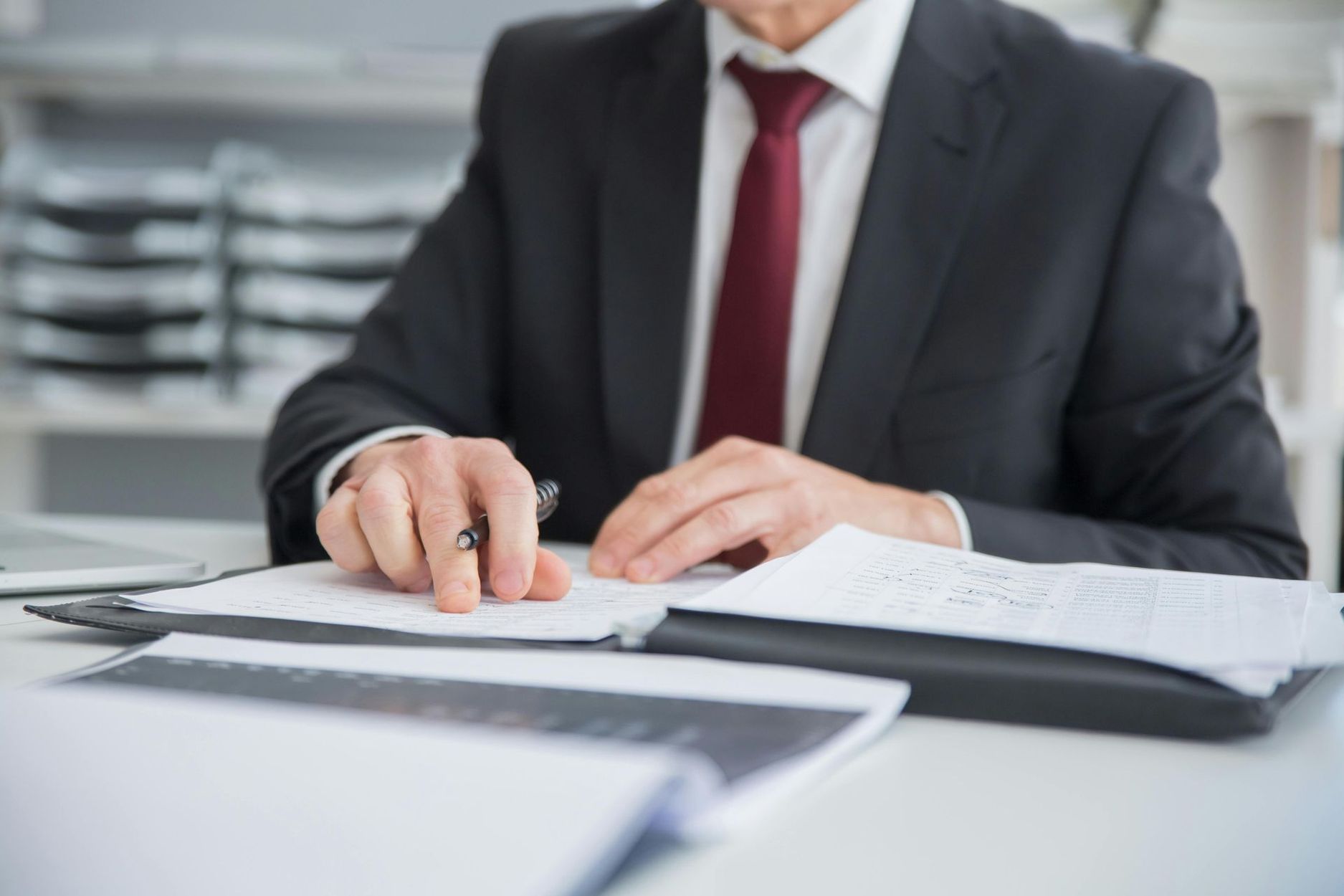 Businessperson in a suit reviewing documents at a desk with a pen and open binder