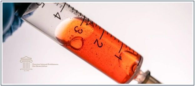 Close-up of a syringe filled with an orange liquid, held by a gloved hand, against a white backgroun