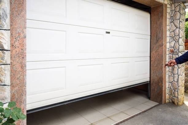 A person is opening a white garage door with a key.