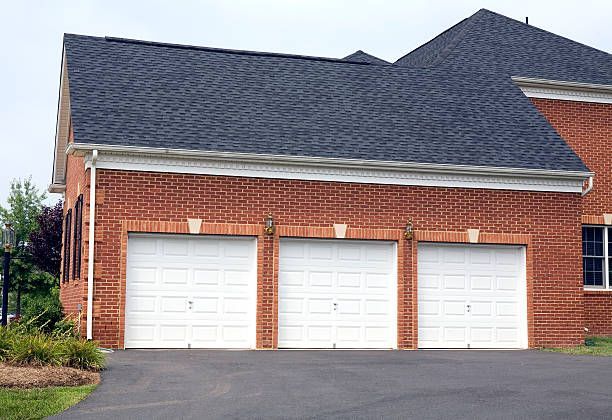 A brick house with three white garage doors and a black roof.