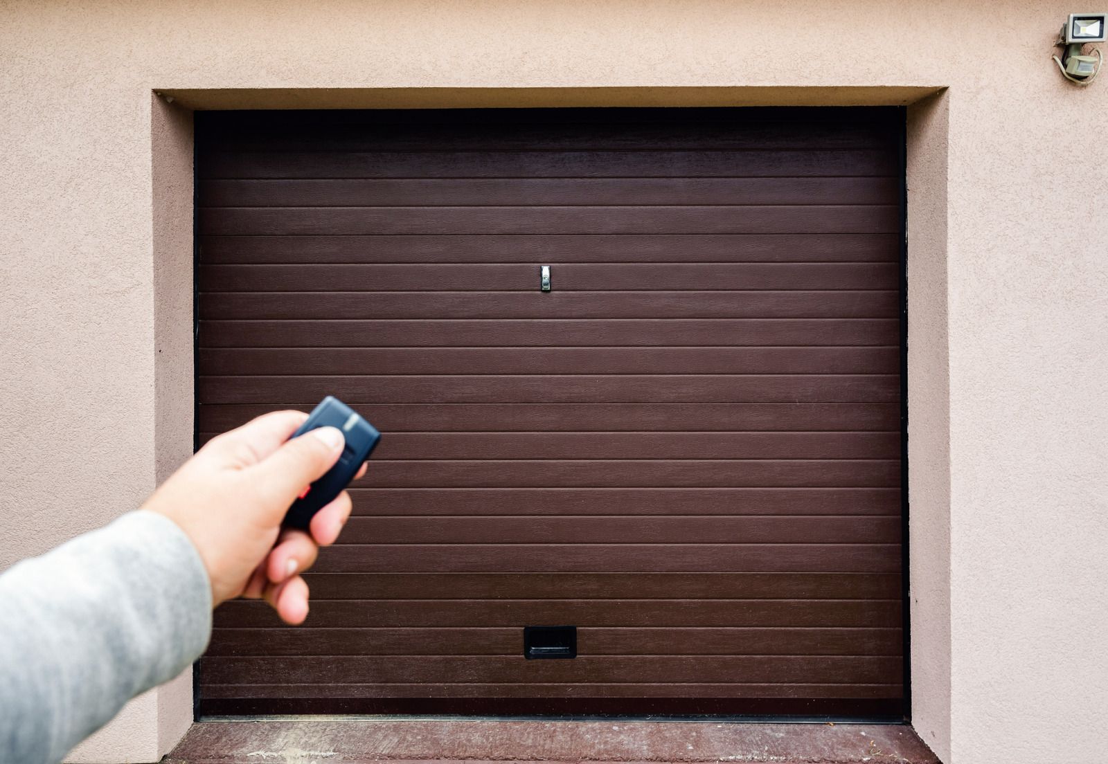 A person is holding a remote control in front of a garage door.