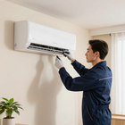 Un técnico, con guantes puestos, utiliza un destornillador para reparar un aire acondicionado blanco montado en la pared de una habitación.
