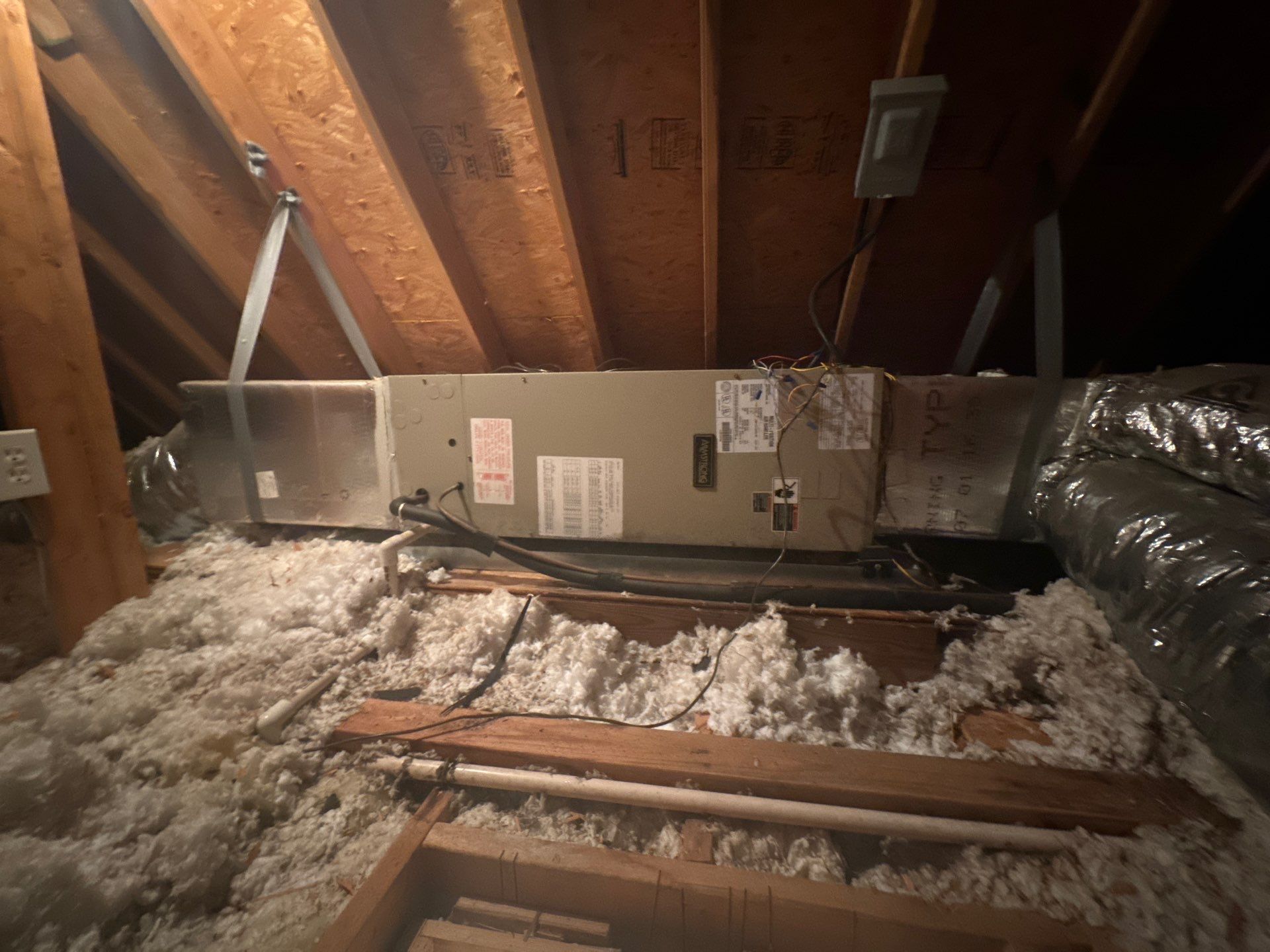 An air conditioner is hanging from the ceiling of an attic.