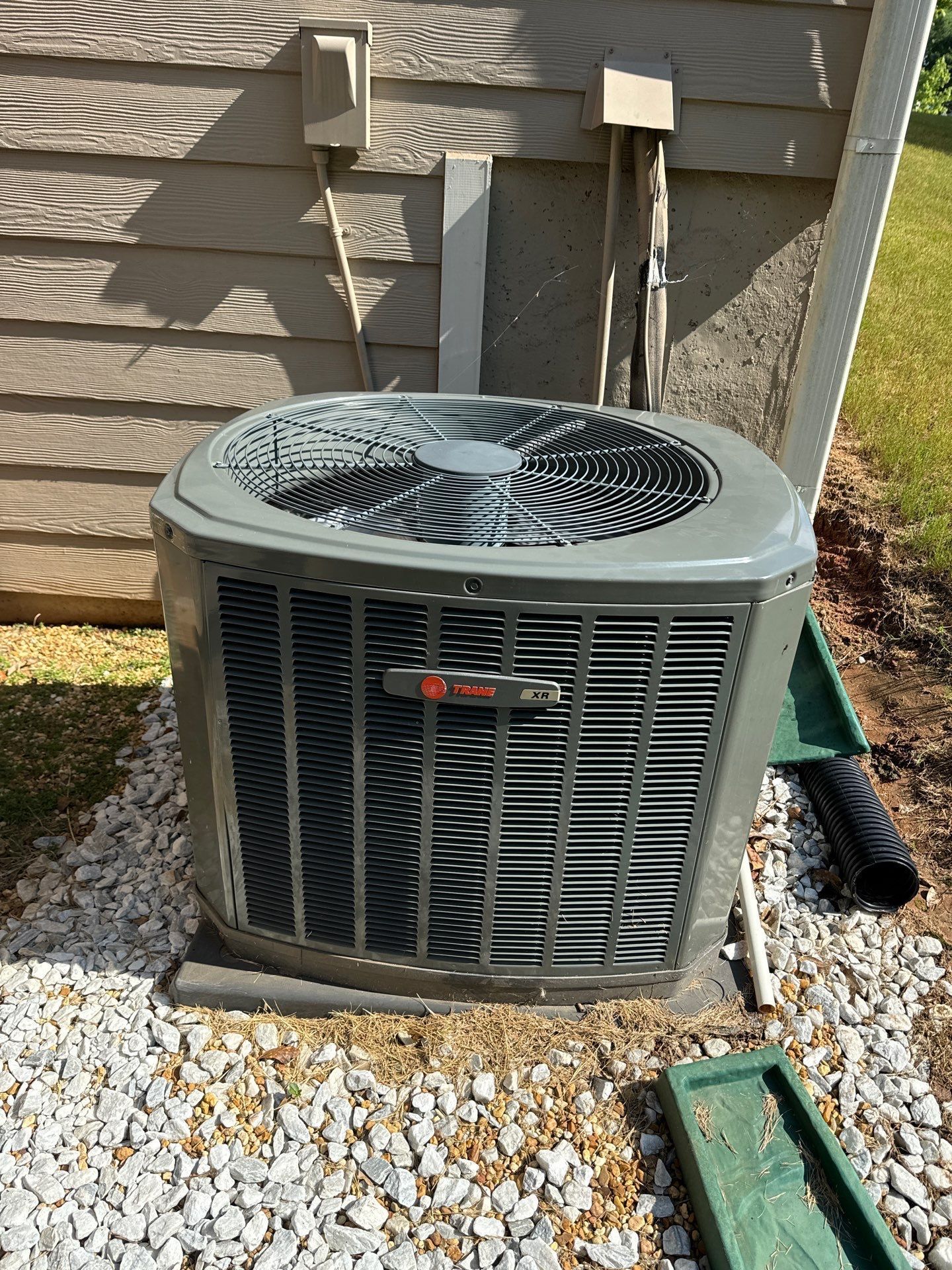 A large air conditioner is sitting on top of a pile of gravel next to a house.