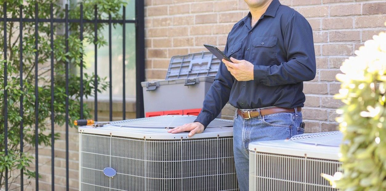 A man is standing next to two air conditioners in front of a brick building.