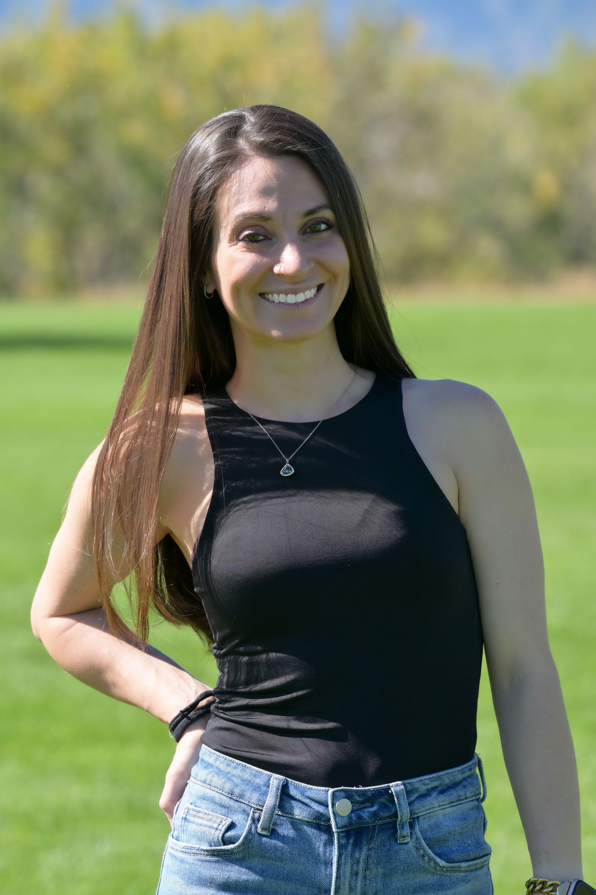 A woman in a black tank top and blue jeans is standing in a field.