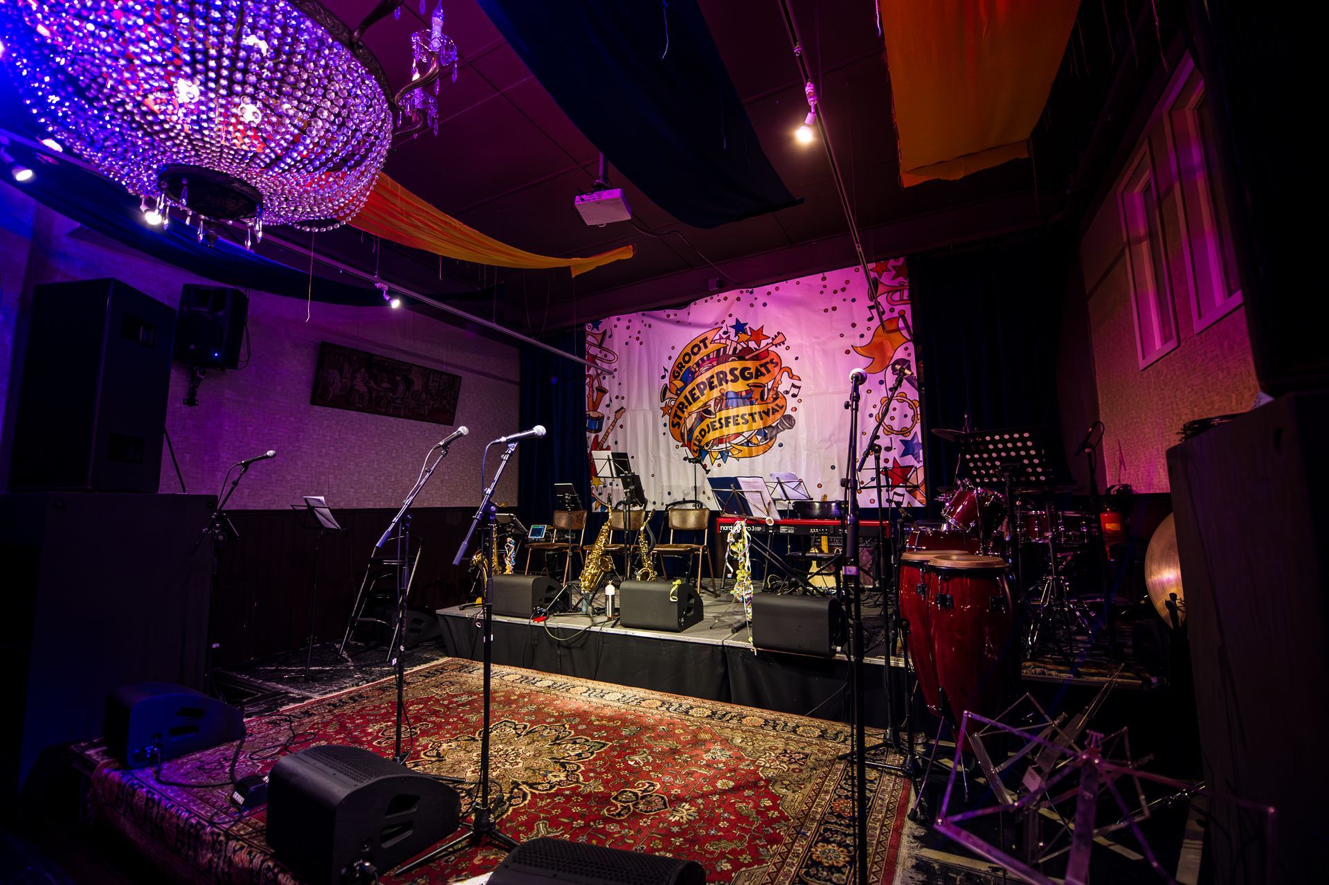 Een podium voor een muziekoptreden, met microfoons, instrumenten en een decoratieve achtergrond in een slecht verlichte zaal.