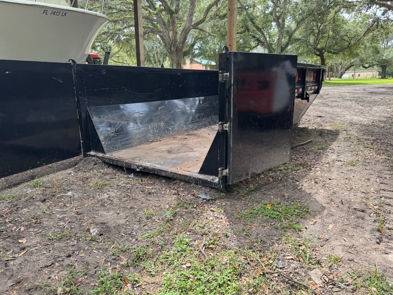 Black metal dumpster with open front on dirt, outdoors.