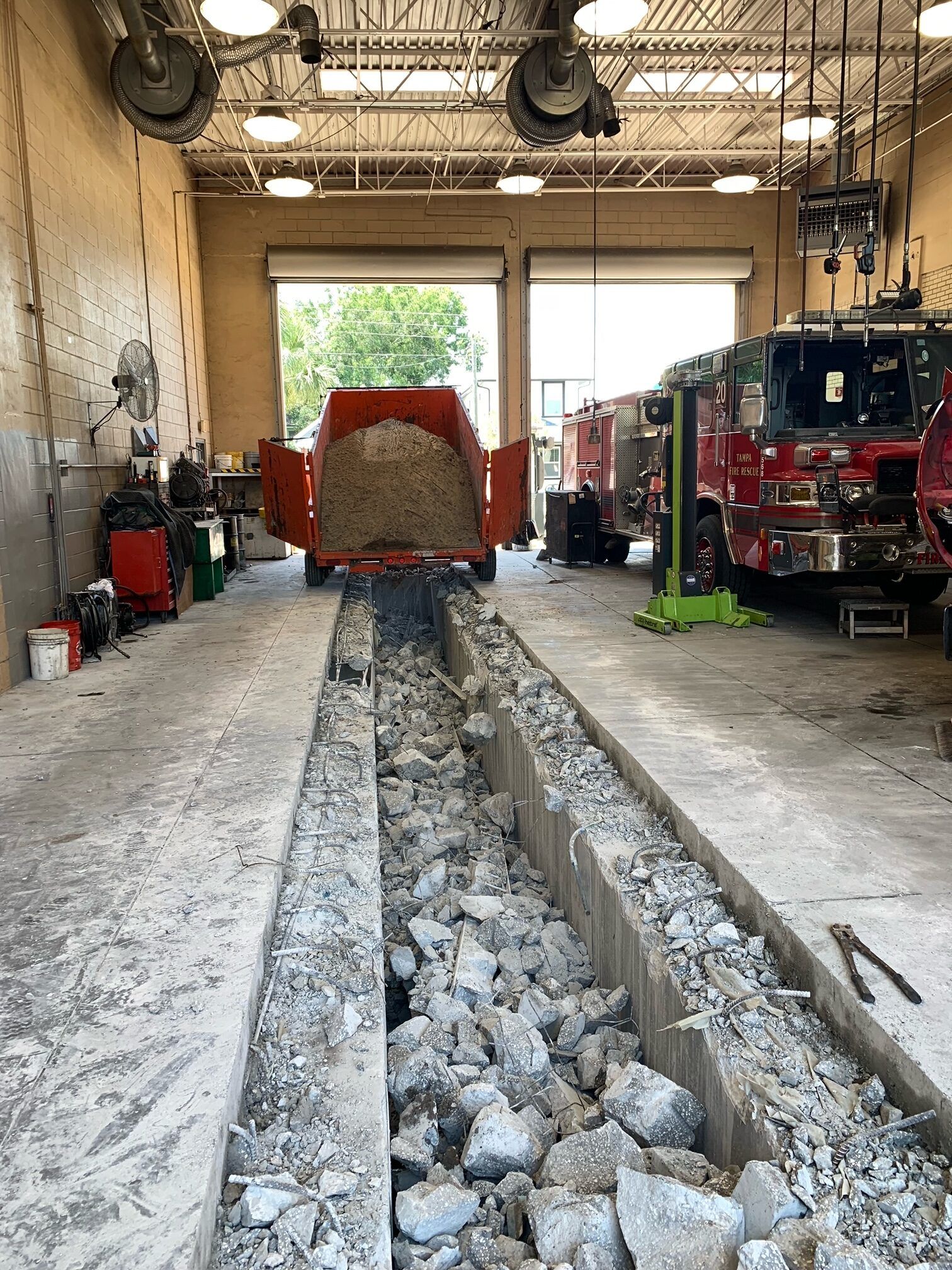 Fire station bay with concrete debris in a trench, an orange dump cart, and firetrucks.