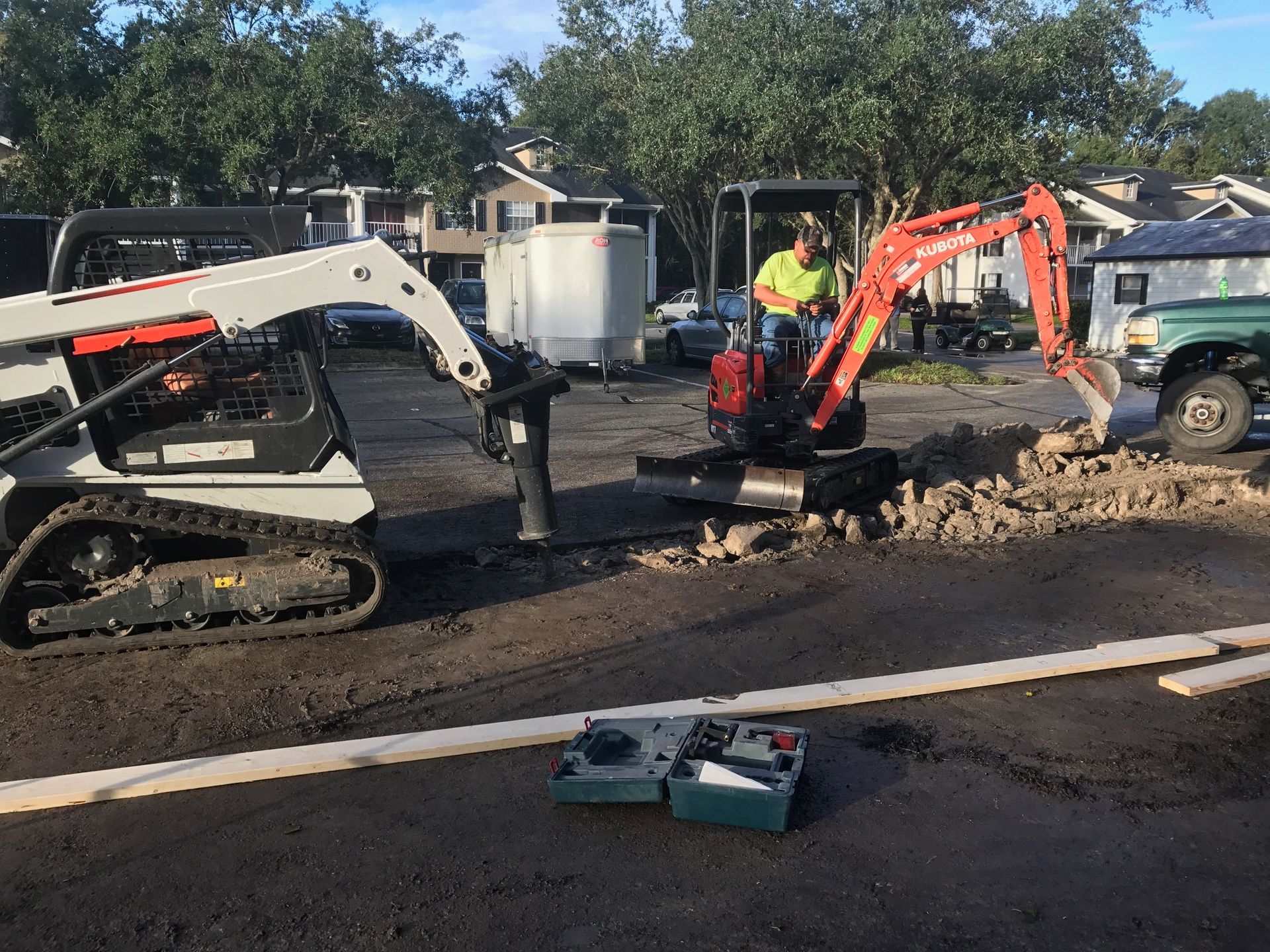 Construction site: excavator digging, Bobcat, workers, asphalt.