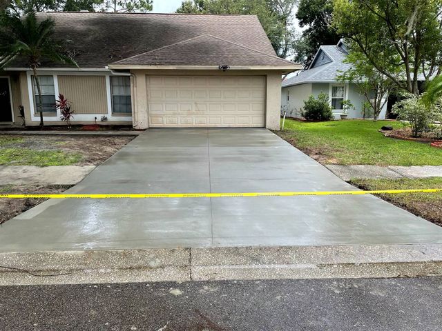 Freshly poured gray concrete driveway in front of a beige house with a closed garage door, yellow caution tape.