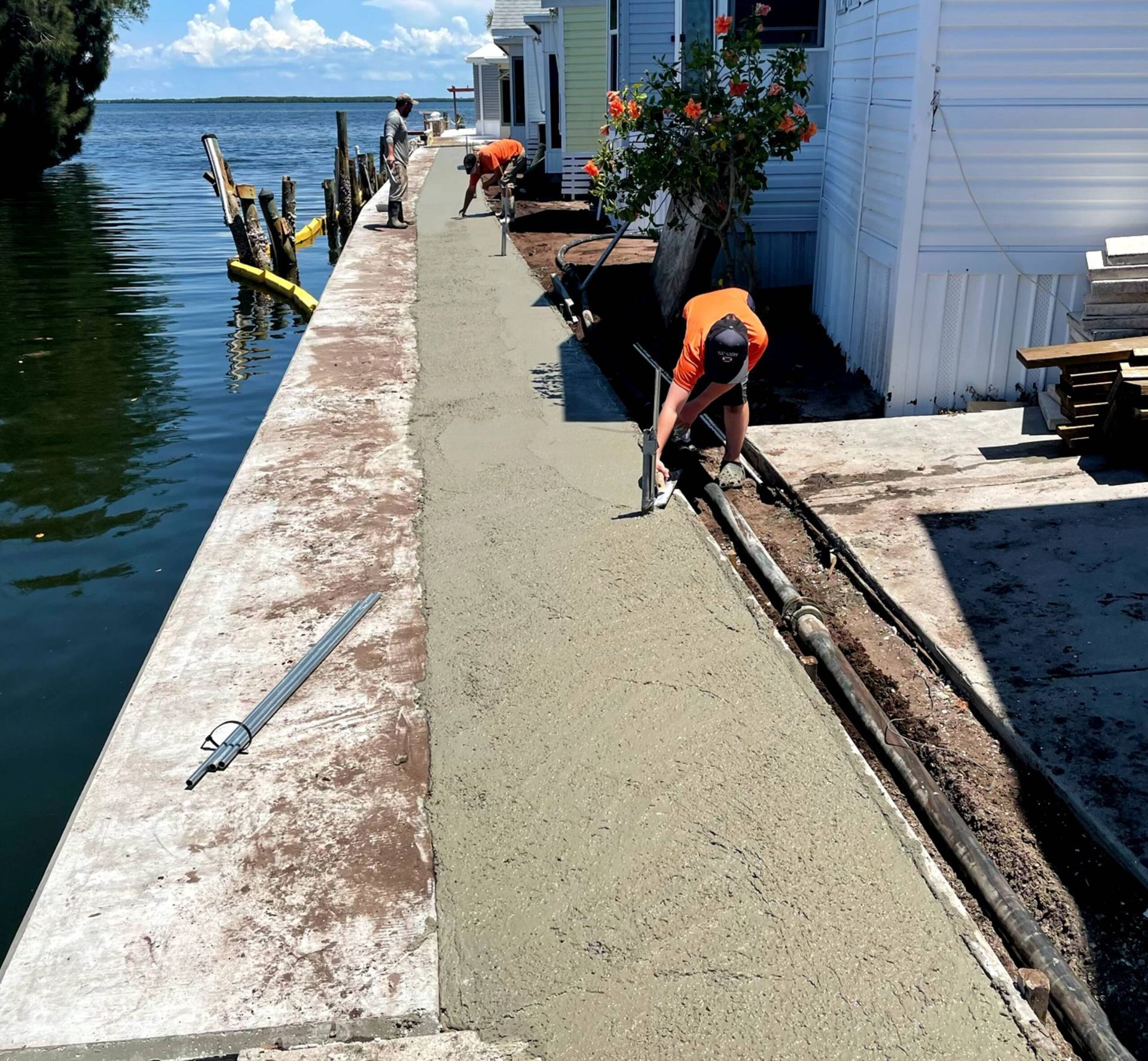 Workers pouring and smoothing concrete on a waterfront walkway. Florida, sunny day.