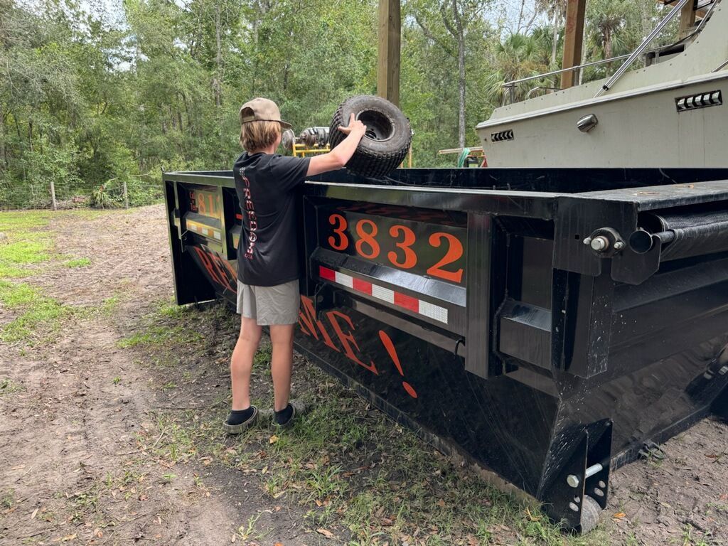 Person loading a tire into a black dumpster trailer labeled 