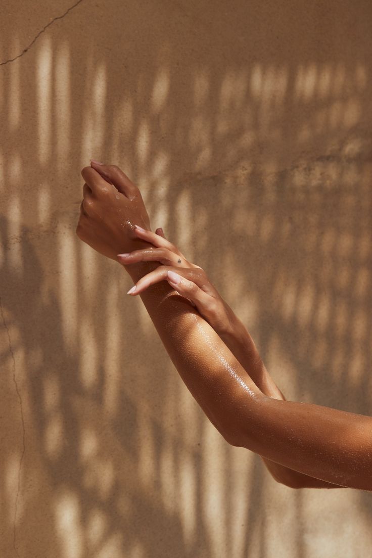 Two Hands, One Arm Raised, Applying Lotion, Against a Beige Wall With Leaf Shadows — Isola Beauty in Corrimal, NSW