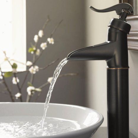 A tall, matte black faucet with an elegant curved handle pours a steady stream of water into a white ceramic basin.