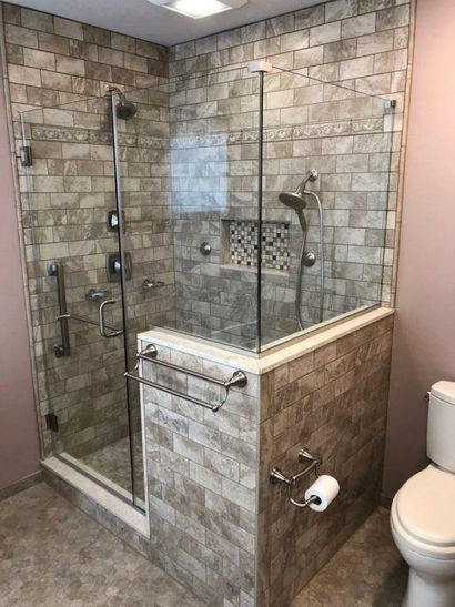 A modern walk-in shower with stone tile walls, a glass enclosure, and a chrome grab bar, next to a white toilet.