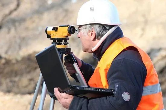 Surveyor in white hard hat and orange safety vest 