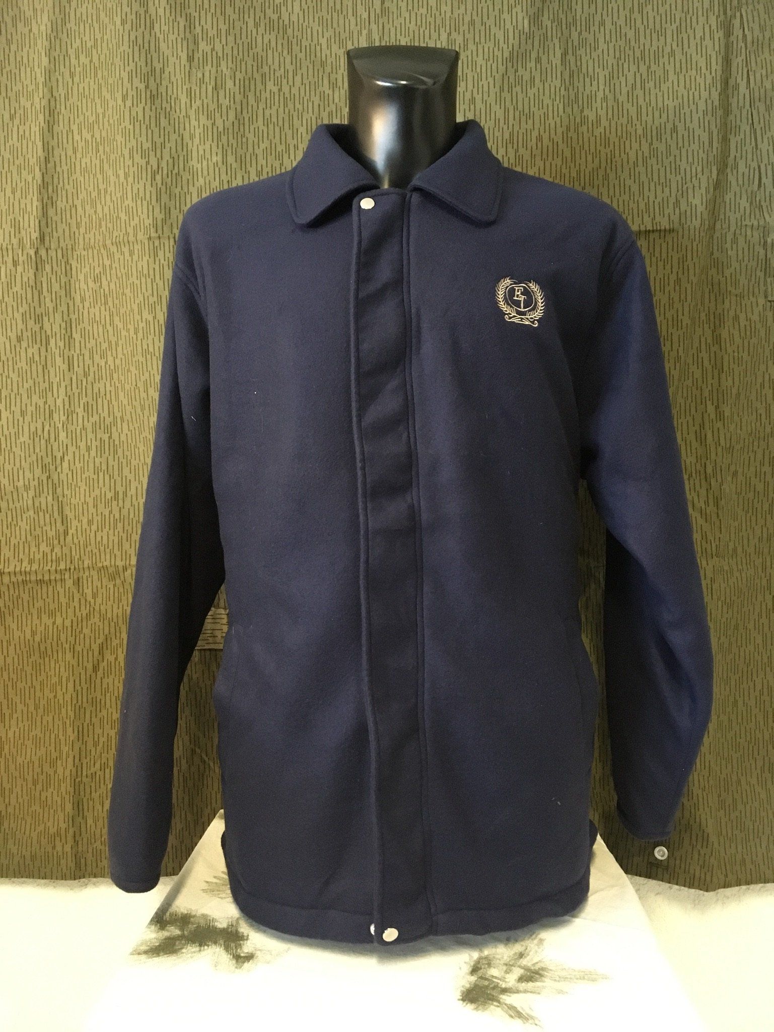 Marineblaue Jacke an einer schwarzen Schaufensterpuppe, mit einem kleinen Wappen auf der Brust.