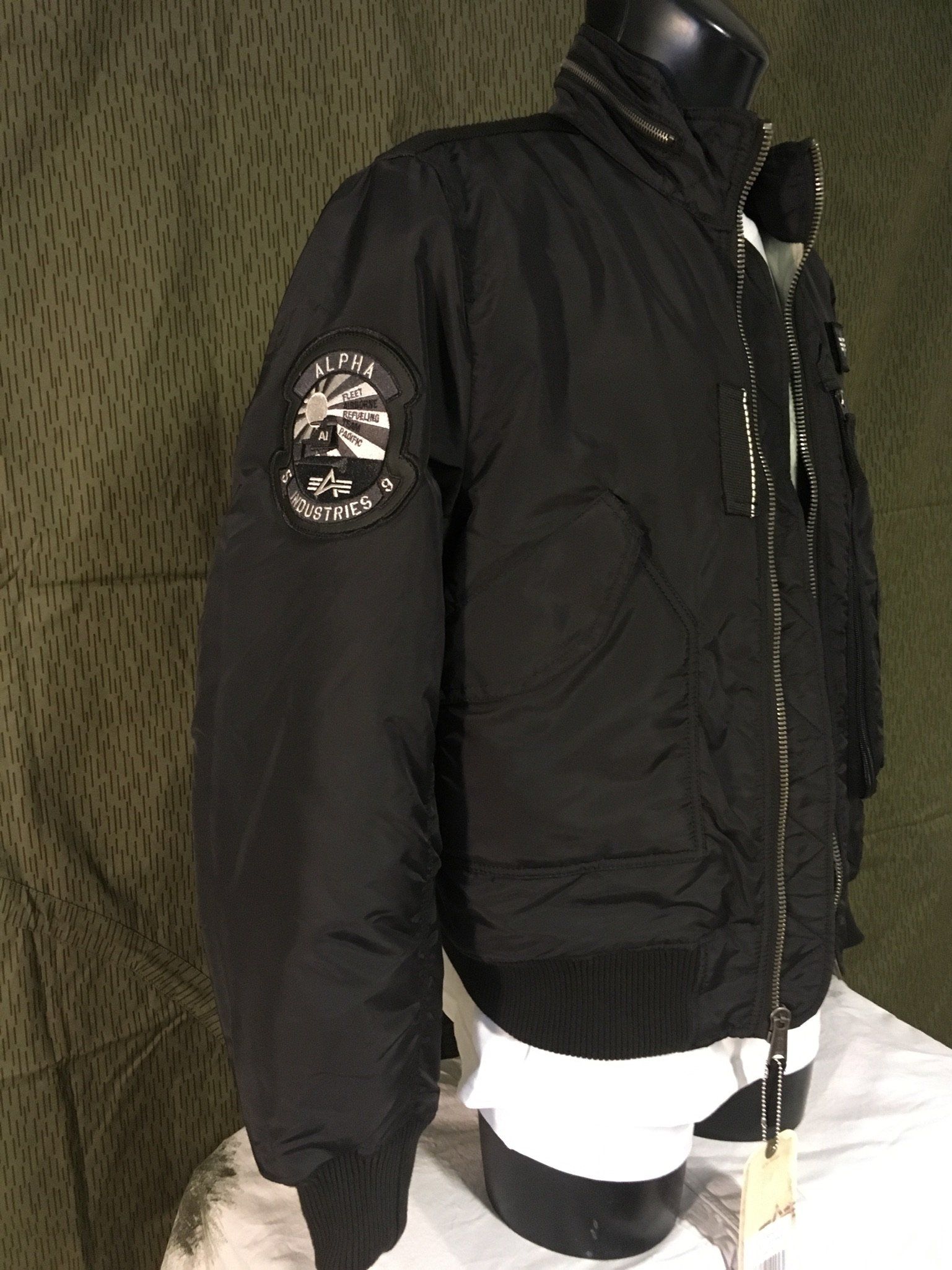 Schwarze Bomberjacke mit einem Aufnäher auf dem Ärmel, ausgestellt auf einer Schaufensterpuppe.