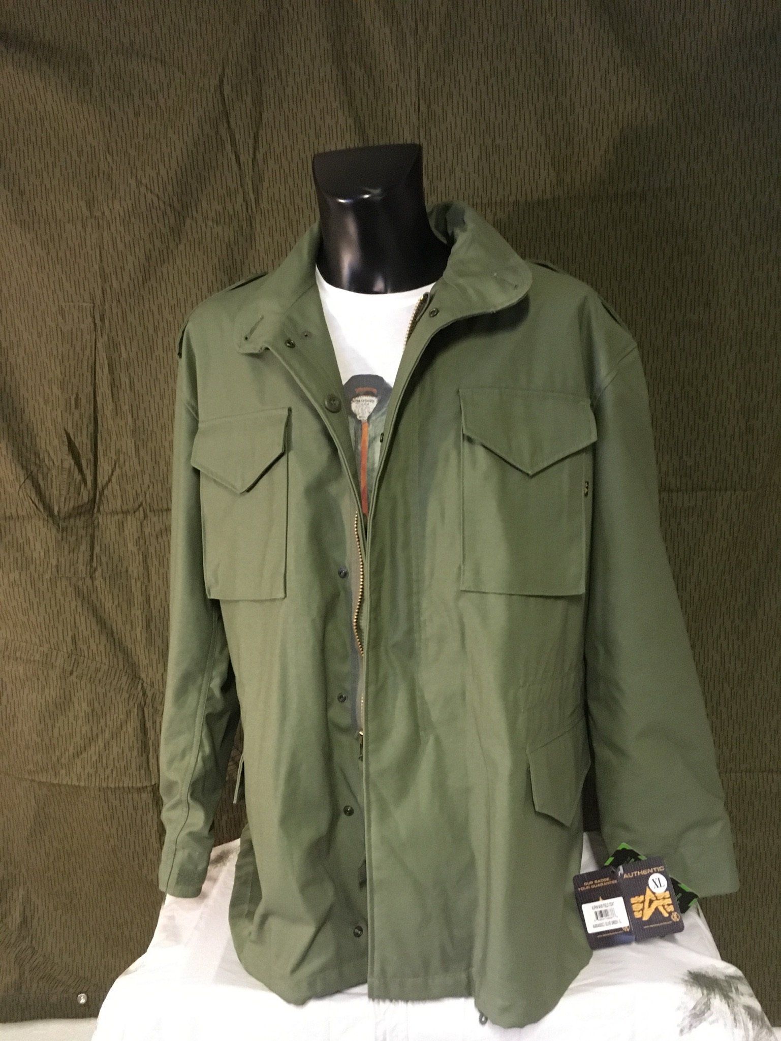 Grüne Jacke im Militärstil auf einer schwarzen Schaufensterpuppe, über einem weißen T-Shirt.