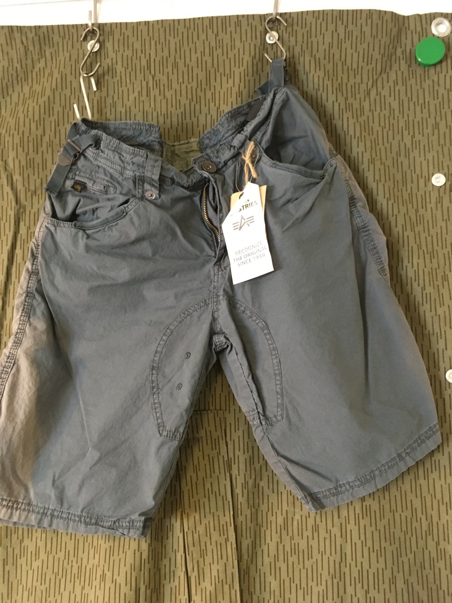 Graue Shorts hängen an Haken mit einem Preisschild vor einem getarnten Hintergrund.