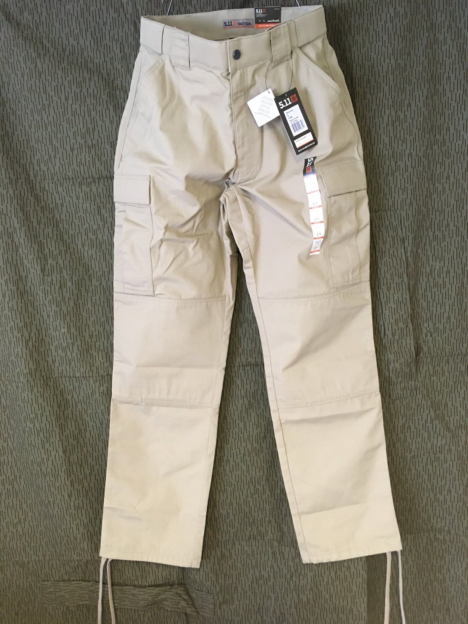 Hellbraune Cargohose mit mehreren Taschen und Kordelzug auf strukturiertem Hintergrund.