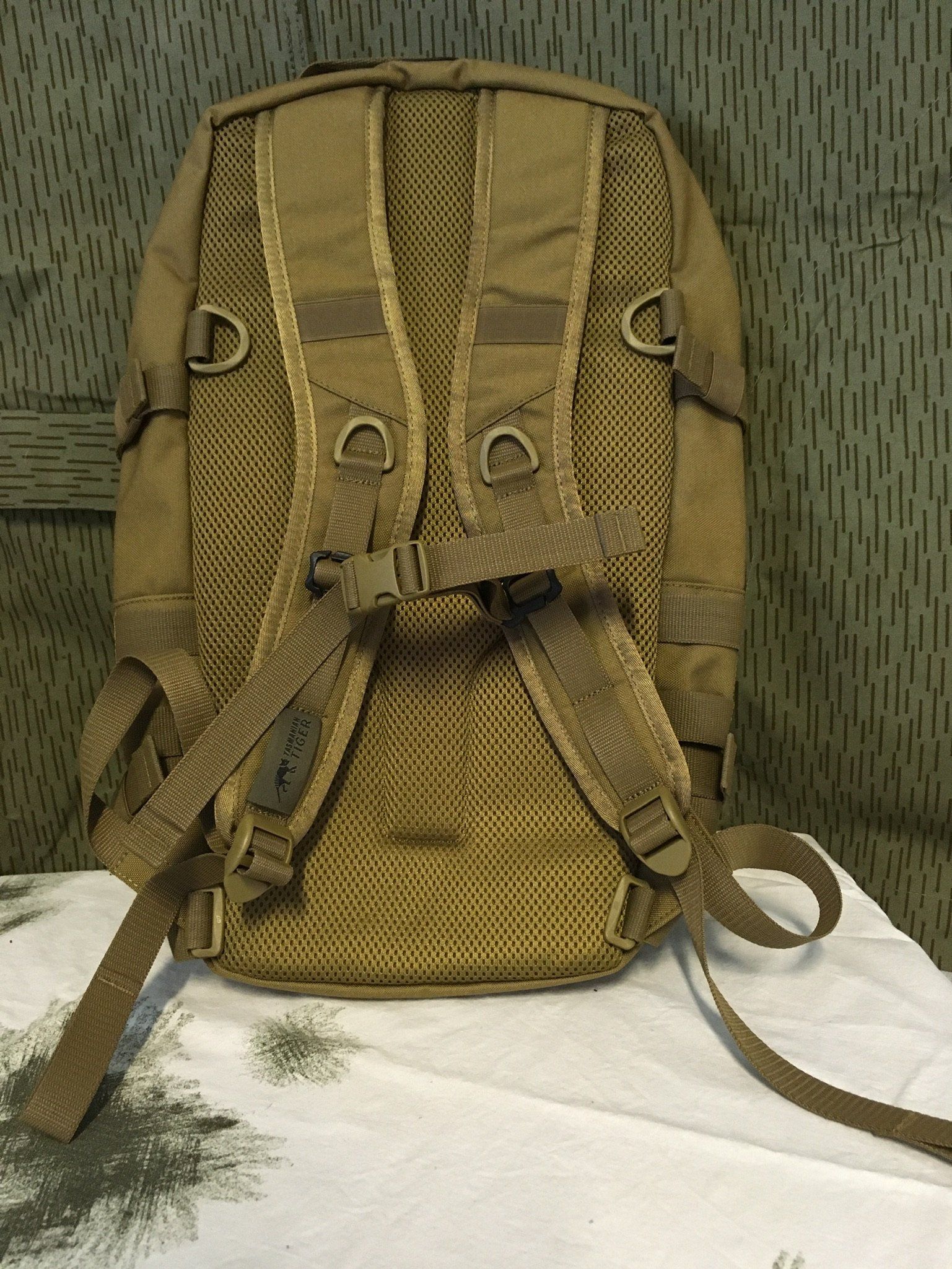 Hellbrauner Rucksack mit gemustertem Hintergrund. Die Rückseite ist mit Netzpolsterung und verstellbaren Riemen versehen.