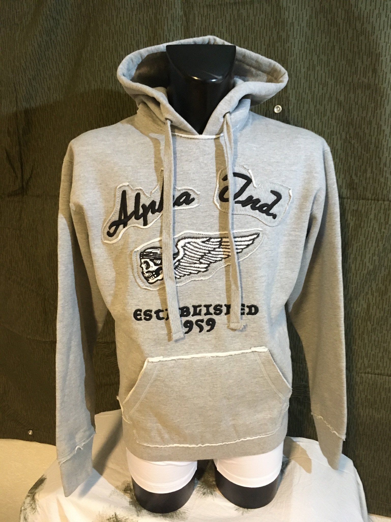 Grauer Hoodie mit schwarzem Schriftzug „Alpha & 2nd“, einem Flügelemblem und „Established 1959“.