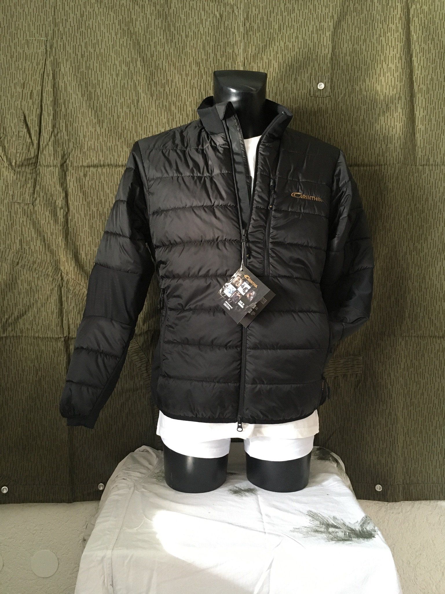 Schwarze Steppjacke an einer Schaufensterpuppe vor einem Tarnhintergrund.