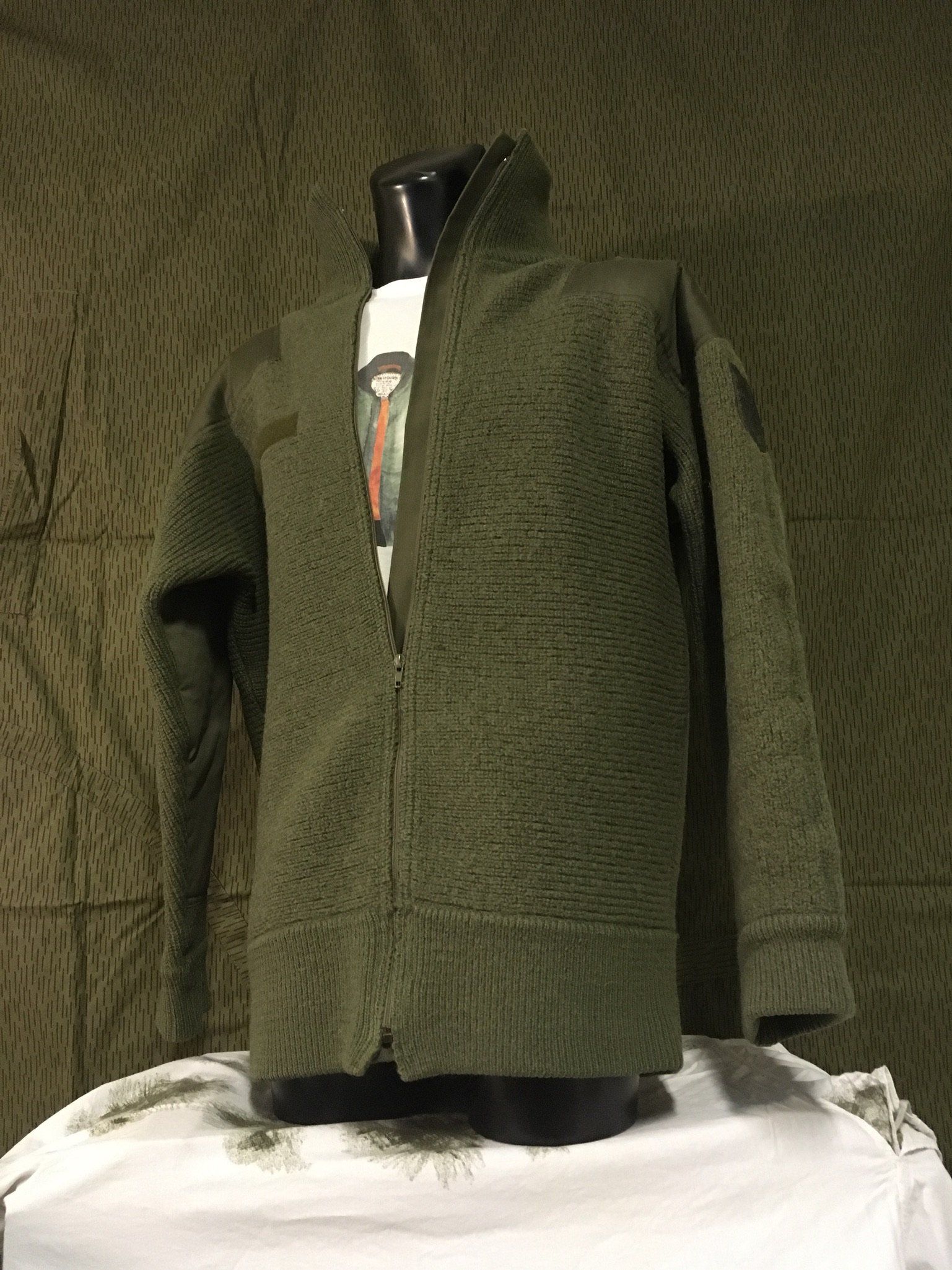 Olivgrüne Jacke auf einer Schaufensterpuppe, Vorderansicht. Mit Reißverschluss und hohem Kragen.