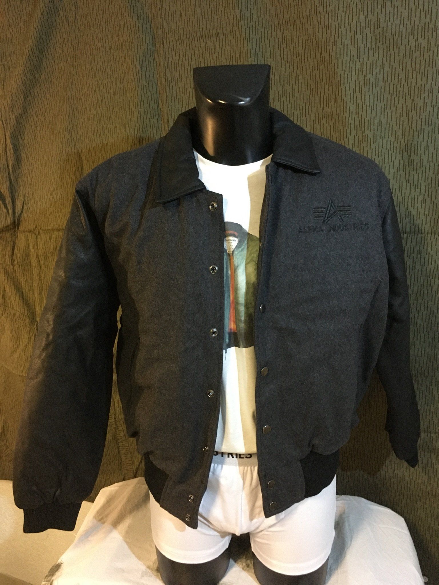 Dunkelgraue Jacke mit schwarzem Kragen und Ärmeln an einer Schaufensterpuppe, über einem weißen T-Shirt und Unterwäsche.