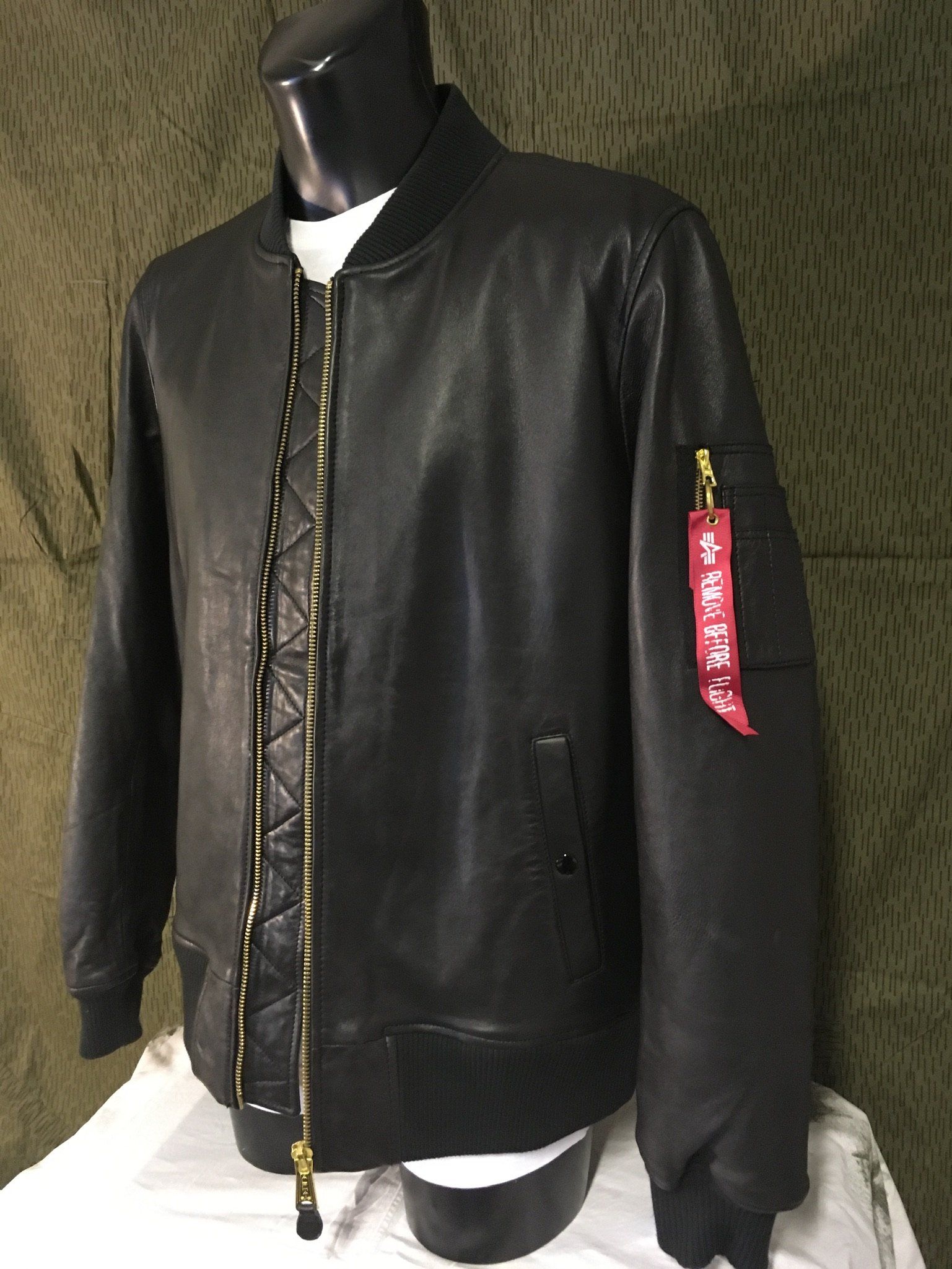Schwarze Bomberjacke aus Leder mit goldenem Reißverschluss und rotem Etikett am Arm.