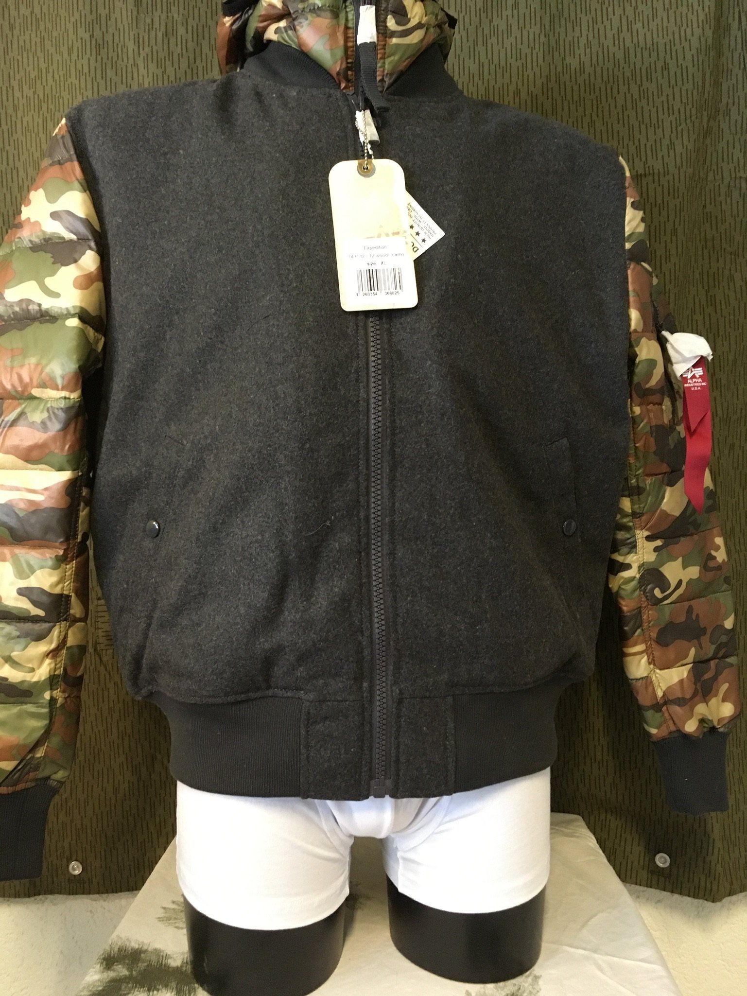 Eine Jacke mit grauem Oberkörper, Tarnärmeln und einem Etikett, ausgestellt an einer Schaufensterpuppe in Unterwäsche.