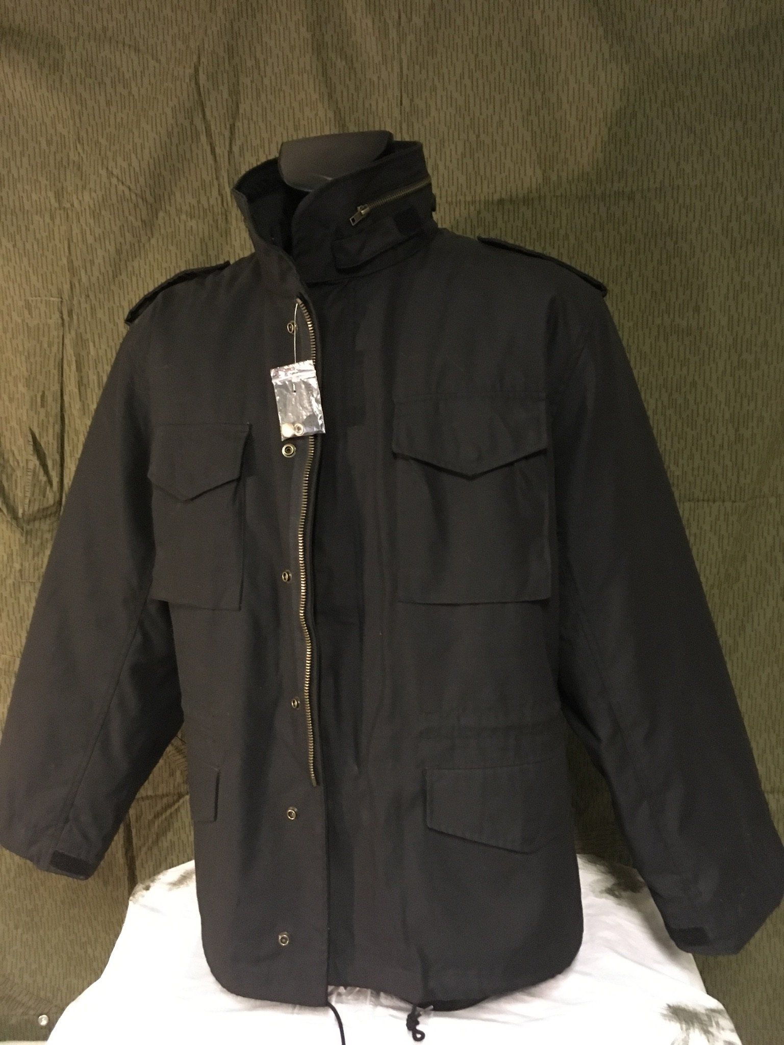 Schwarze Jacke im Militärstil an einer Schaufensterpuppe, mit Reißverschluss und Taschen.