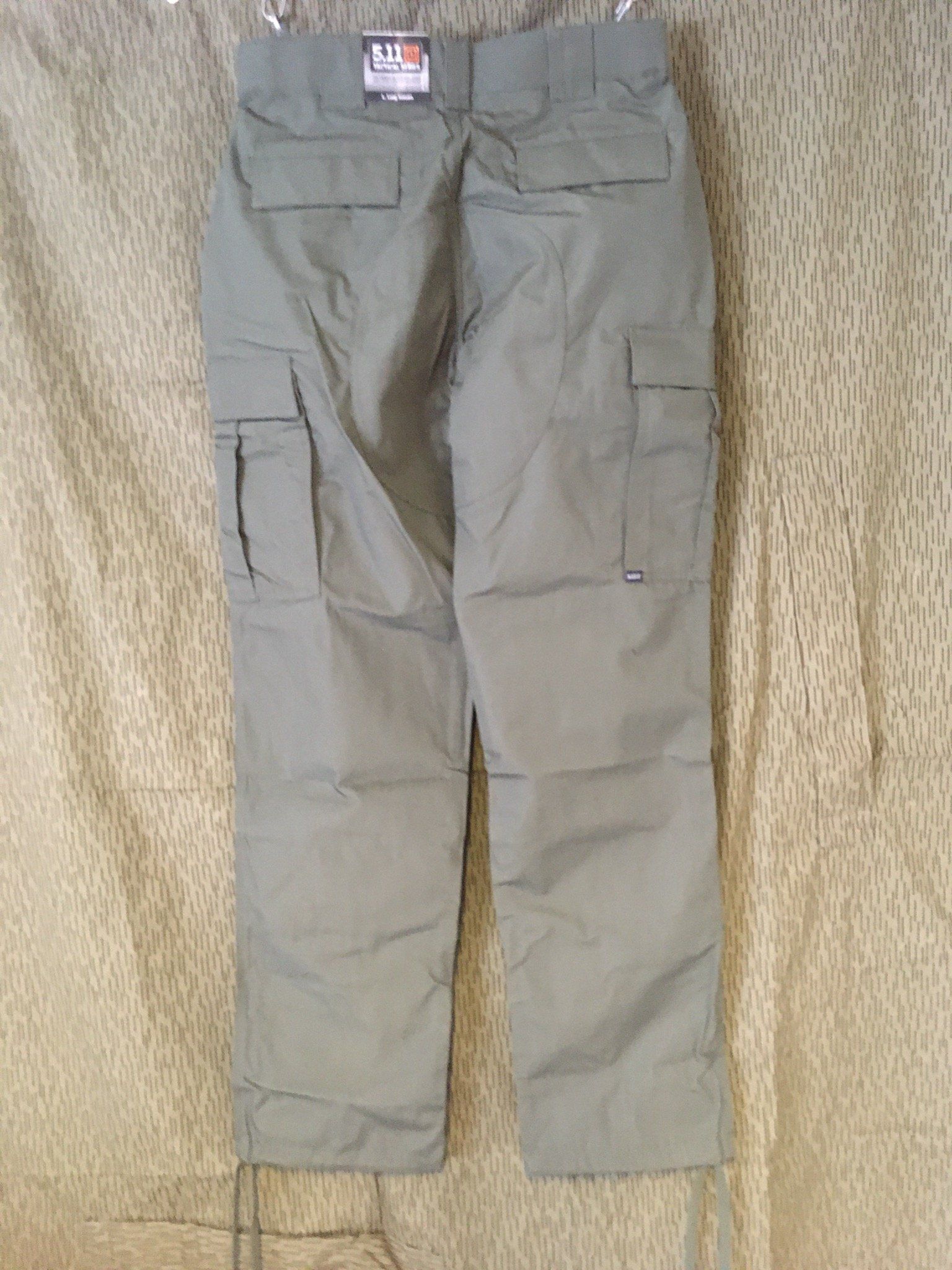Rückansicht einer grauen Cargohose, die vor einem gemusterten Hintergrund hängt.