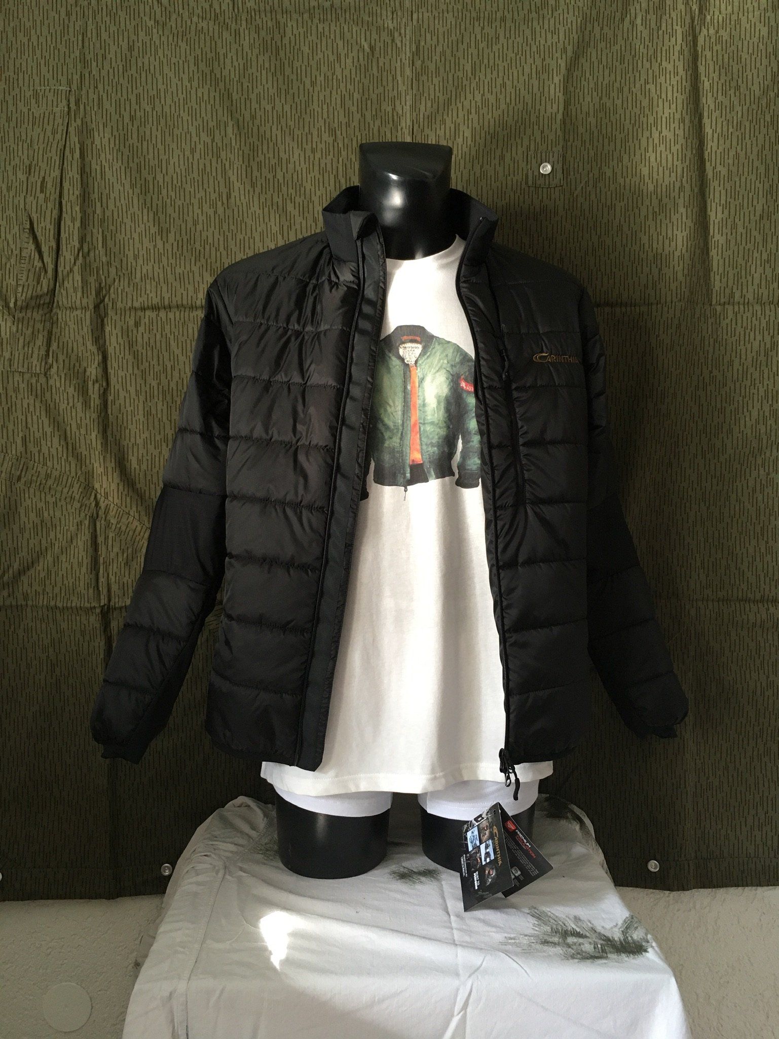 Schaufensterpuppe in schwarzer Pufferjacke über weißem T-Shirt. Dunkler Hintergrund, auf einem Tisch stehend.