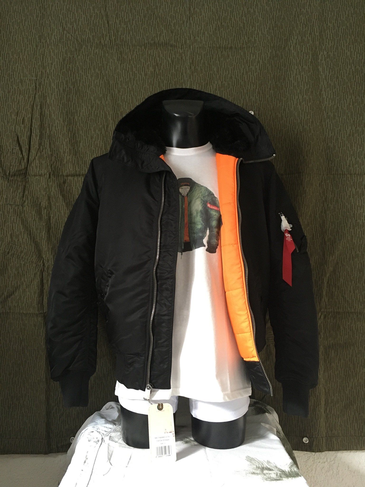 Schwarze Bomberjacke mit orangefarbenem Futter und Kapuze über einem weißen T-Shirt auf einer Schaufensterpuppe.