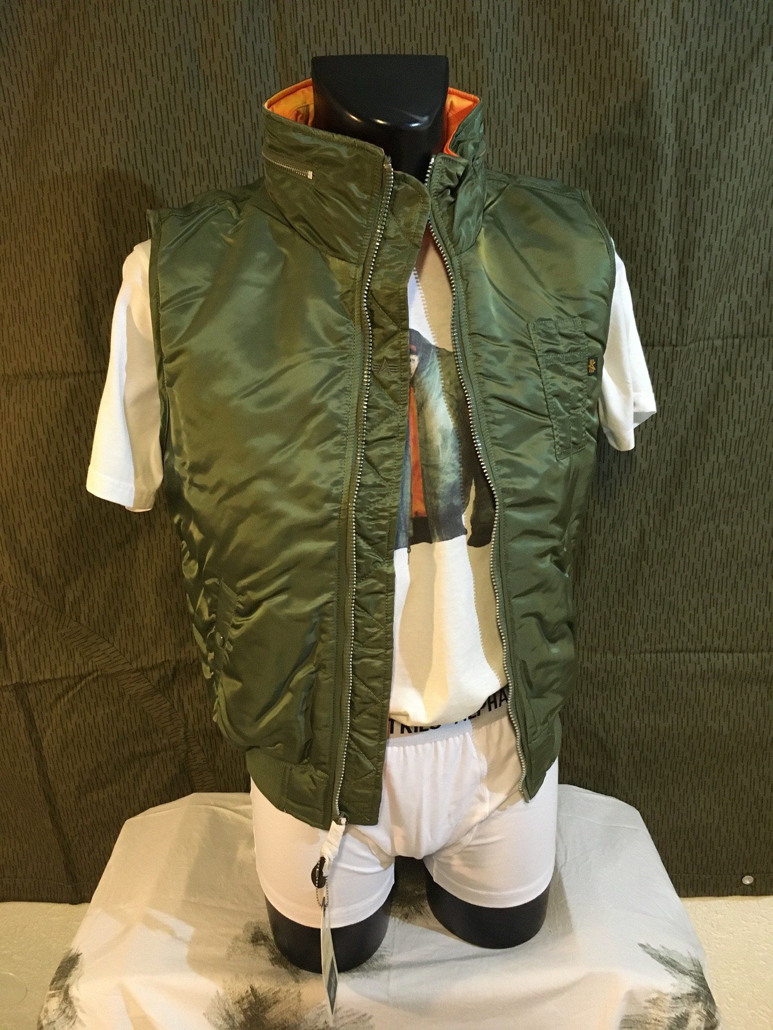 Grüne Steppweste über weißem T-Shirt und Unterwäsche auf einer schwarzen Schaufensterpuppe.