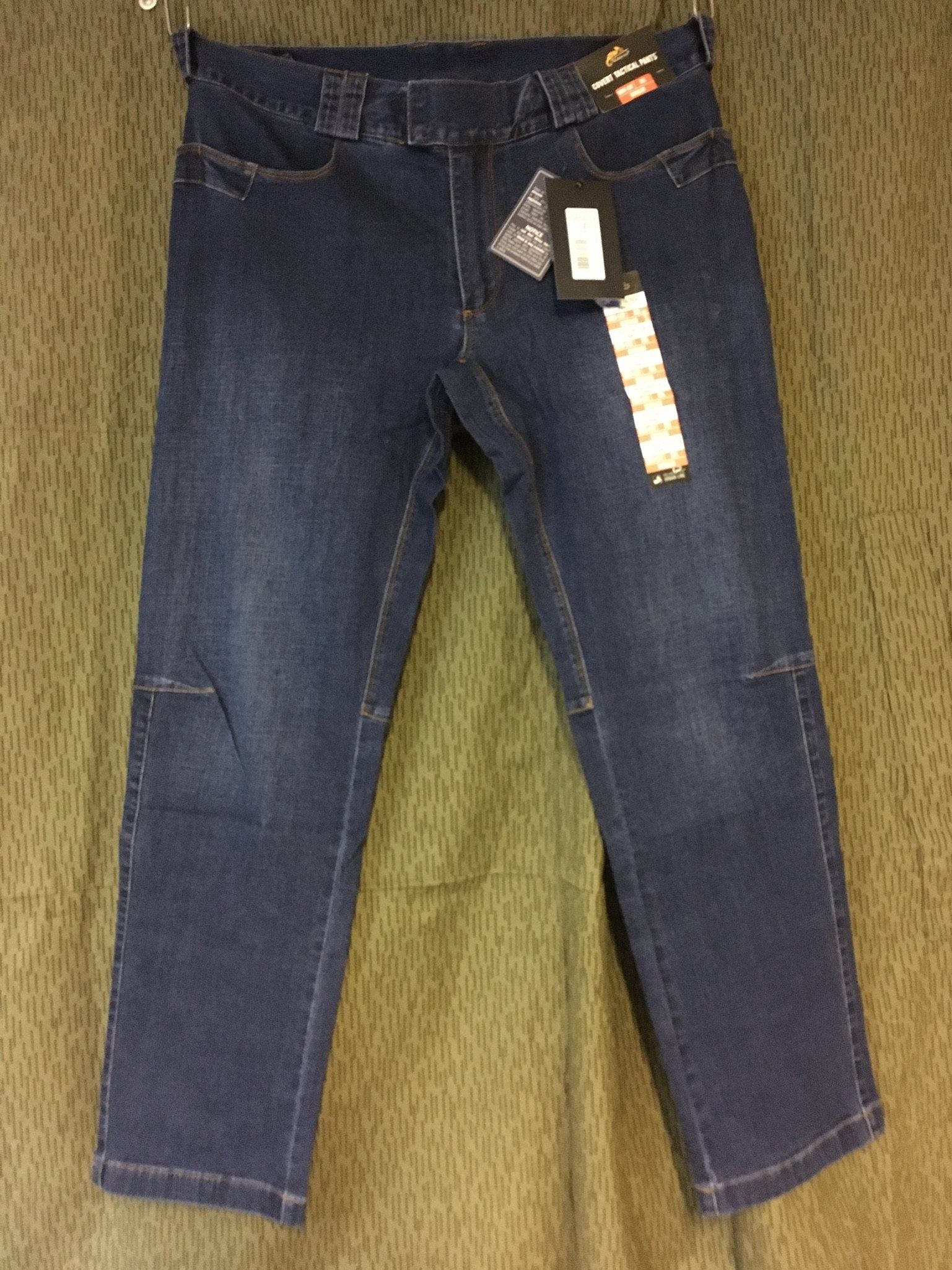 Dunkelblaue Jeans mit Knieflicken und Preisschild, die an einem Ständer hängen.