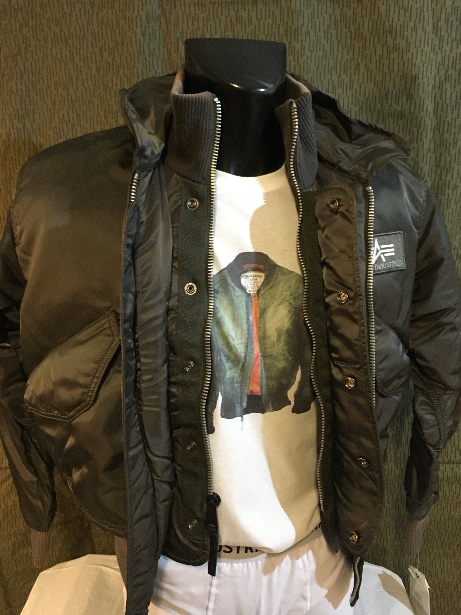 Schaufensterpuppe trägt eine dunkelgrüne Bomberjacke über einem T-Shirt mit Jackenaufdruck.