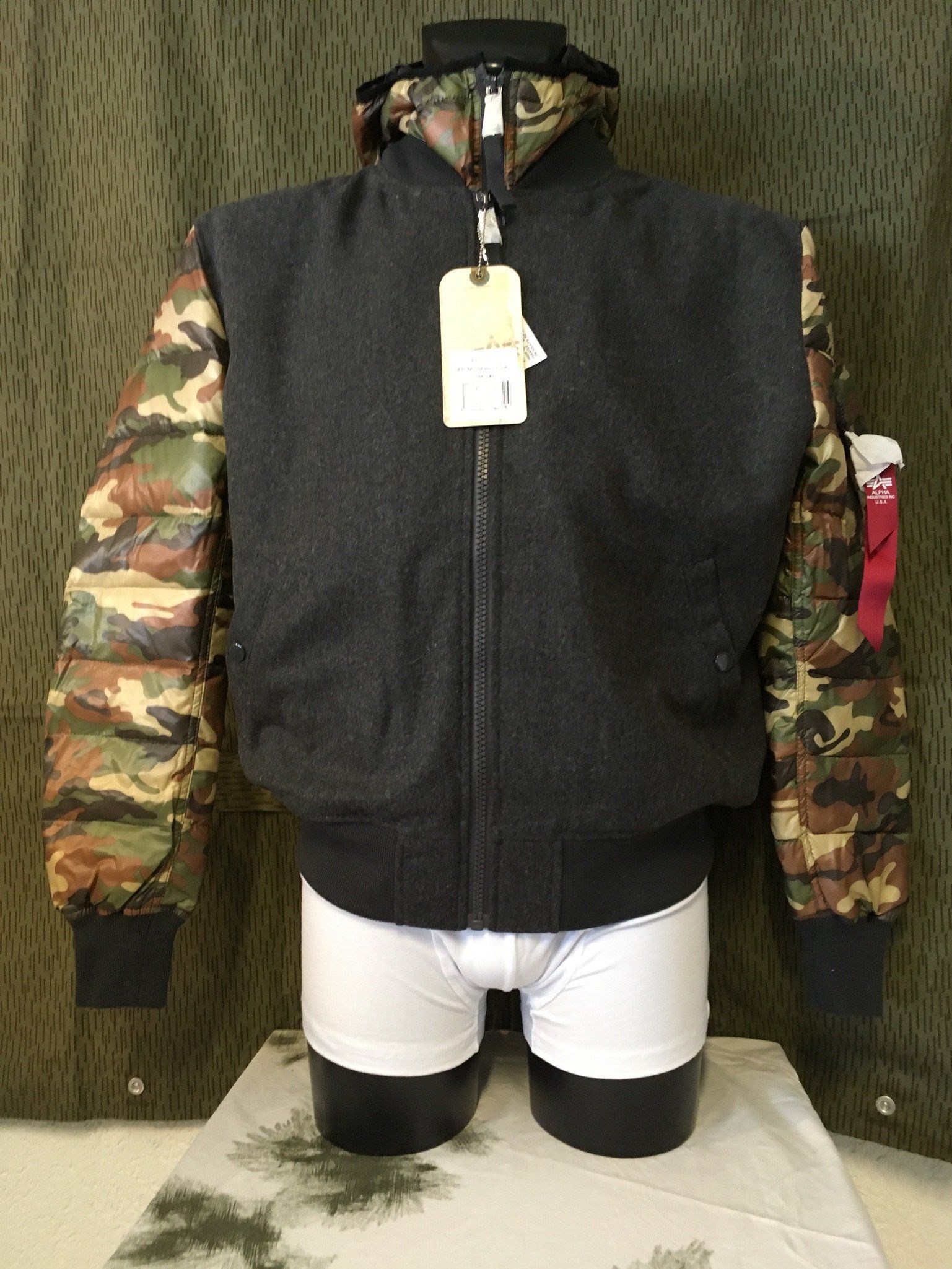 Dunkelgraue Jacke mit Camouflage-Ärmeln, an einer Schaufensterpuppe in weißer Unterwäsche.